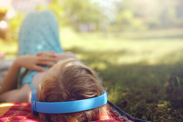 Young blonde haired girl lies peacefully on a late summer meadow with blue headphones on - view...