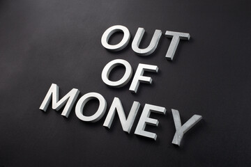 the words out of money laid with white brushed metal letters on flat black surface with diagonal...