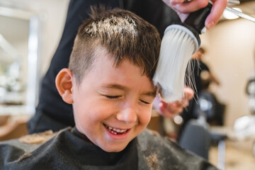 Crop barber removing cut hair from cheerful boy
