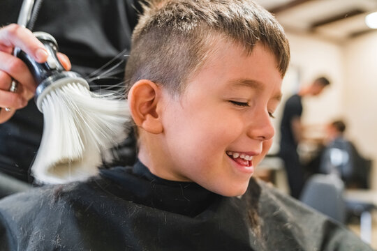 Crop barber removing cut hair from cheerful boy