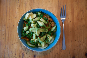fried chickpeas with avocado, cucumber, paprika, carrots parsley in a blue bowl on a rustic wooden table