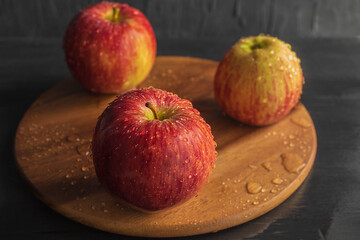 On a wooden round board are red ripe apples with drops of water