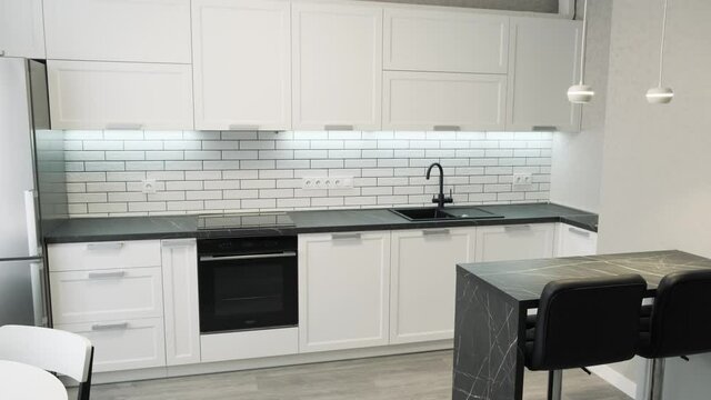 Elegant modern kitchen with white walls. Light interior of a white kitchen in a compact apartment, black and white furniture. Ceramic tiles on the wall and wooden countertop 4k