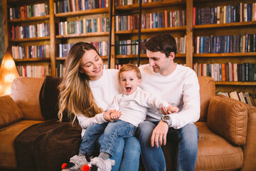 Happy family on sofa near bookcase and Christmas tree in evening. Cozy family atmosphere at christmas time . Enjoyng love hugs, holidays people. Togetherness concept. Home holiday living room