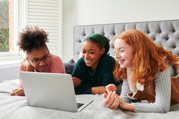 Teen girls using a laptop on a bed