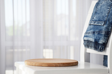Round wooden board with free place for your product and blue denim jeans stacked on white chair...