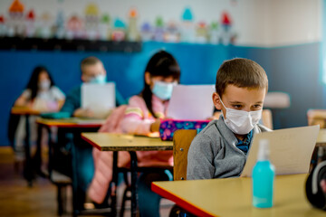 Elementary schoolchildren wearing a protective face masks  in the classroom. Education during epidemic.