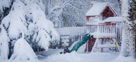 Young boy  using a slide on a backyard play set in the middle of a snowy blizzard.
