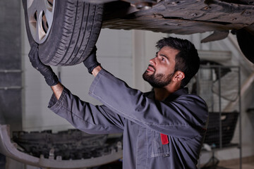 Fototapeta na wymiar young caucasian auto mechanic in uniform is examining car wheels in auto service. male is concentrated on work