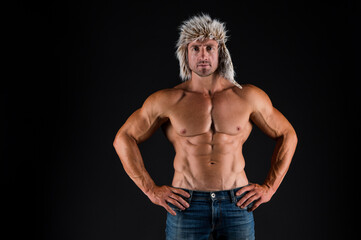 Fototapeta na wymiar Bodycare with fitness and sport. Man with muscular torso. Bodybuilder in fur hat and jeans dark background. Bodycare and wellness. Health and diet