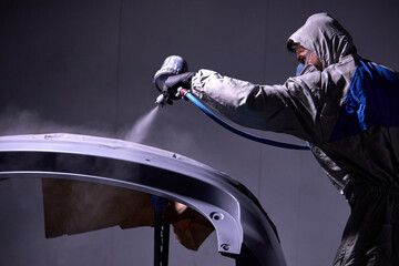 young confident caucasian auto mechanic man spraying varnish at car, in protective mask and gloves at work. automobile, car industry. wash and coating business with ceramic coating polishing