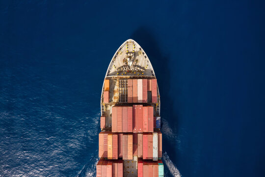 Aerial top down view to a cargo vessel loaded with containers traveling over blue sea