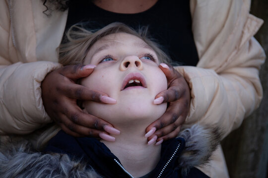 A black girl with long nails caresses the face of a young white girl.