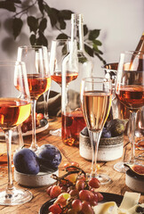Rose wine glasses and bottles on table served for festive dinner party with different kinds of appetizers and fruits