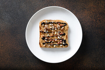 Crispy toast with peanut paste in white plate isolated on brown. View from above.