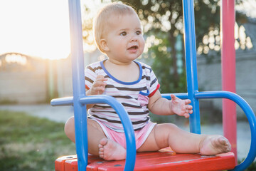 Blonde baby sitting on a swing at sunset