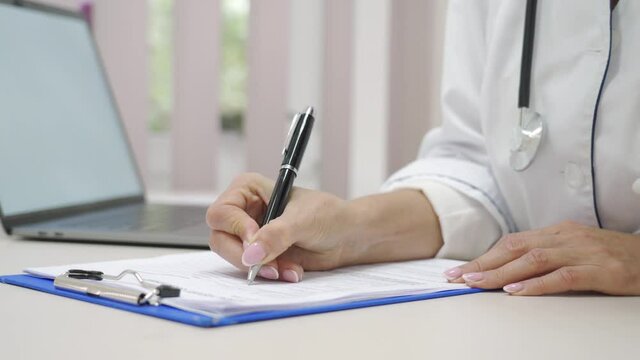 Close-up female doctor hands taking notes and filling medical questionnaire.