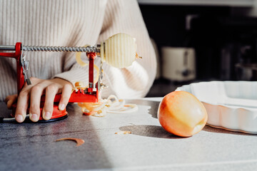 Close up of girl hands slicing aplle using apple peeler corer slicer machine. Child cooking charlotte or apple pie