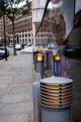 Grey street bollard and lighting with blurred background street scene.