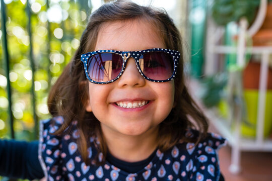 Stylish happy small girl in sunglasses on terrace in kindergarten