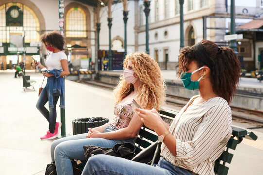 People in face masks sitting on a train platform