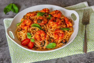 Pasta in tomato sauce with shrimps, olives, basil and garlic on a beautiful plate close-up. 