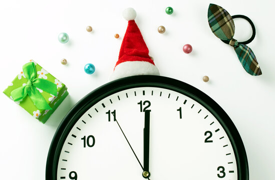 A white clock in a red Santa hat shows five seconds to midnight, on a white background with Christmas decorations. Countdown to the New year