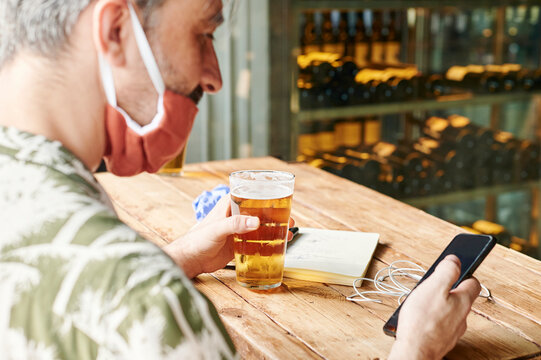 Man in a face mask checking his phone at a bar