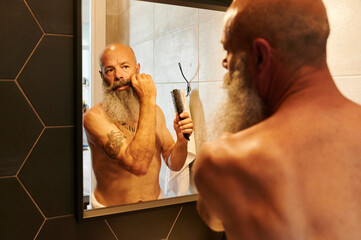 Mature man styling his beard in a mirror