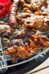 Chicken, sausages and red bell pepper being barbequed