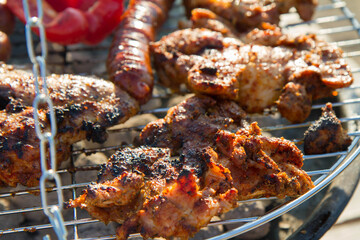 Chicken, sausages and red bell pepper being barbequed