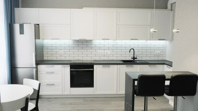 Simple well designed modern white wooden kitchen interior. Light interior of a white kitchen in a compact apartment, black and white furniture. Ceramic tiles on the wall and wooden countertop 4k