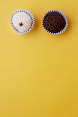 Beijinho and Brigadeiro on yellow background, with copy space. Brazilian handmade candies. Vertical photo.