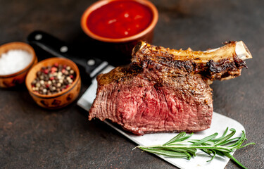 Baked beef on the bone with spices on a meat knife against a stone background