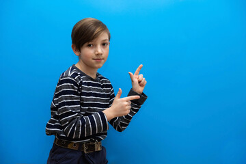 The boy points his fingers to the side. Photo of a cheerful boy on a blue background. Photo with a child for a banner of promotions, discounts