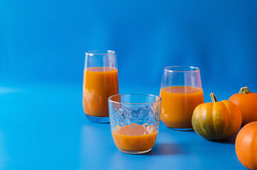Natural pumpkin juice with pulp in glass glasses on a blue background, decorative orange pumpkins stand nearby with copy space, healthy diet food concept