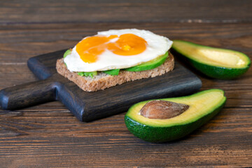 Toast with egg and avocado on a cutting board and halved avocado on a wooden table. Healthy food.