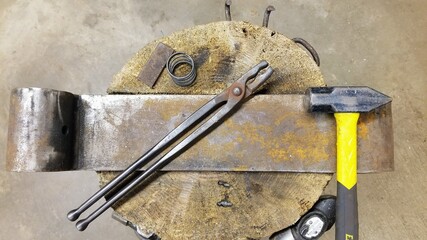Beginner blacksmith anvil setup (railroad tie in a stump) with wolf jaw tongs and a 3.5 lb. hammer and small steel (a spring and small billet).