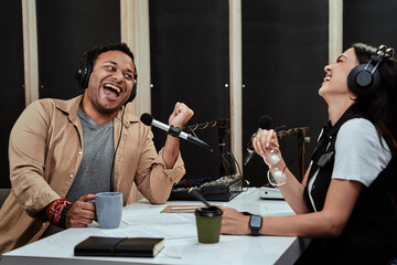 Portait of two radio hosts, man and woman laughing while talking with each other, moderating a live...