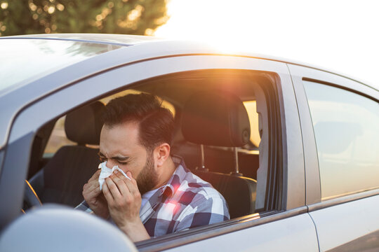 Young man sneezing while driving car. Healthcare, virus, allergy concept.