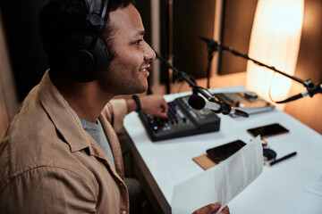 Portrait of young male radio host going live on air, talking in microphone, holding a script paper...