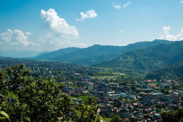 A panorama of successive mountain slopes, lost in a haze, against a background of blue sky and white cumulus clouds.