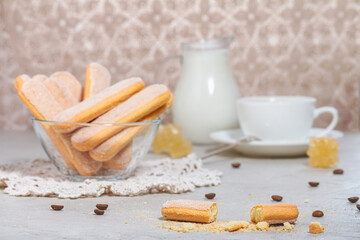Traditional italian savoiardi or ladyfingers biscuits in a glass bowl and pieces of cookies and sugar on the table. Selective focus