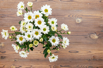 A bouquet of white bush chrysanthemums on a wooden table in the upper left corner.