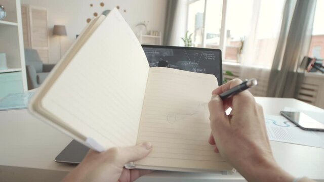 POV first-person of female hands drawing geometrical figure from online lecture running on laptop in front on desk in office at home