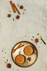 Fototapeta na wymiar Hot fragrant masala tea in small copper cups on a round tray.On a grey stone background with spices, top view with space