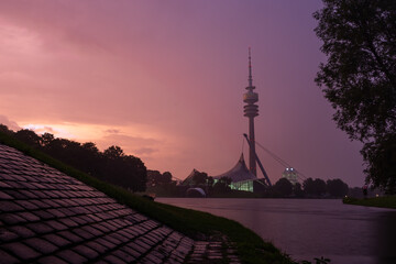 Sunset in the Olympiapark in Munich with view on the lake and tower. Skyscraper behind a lake in...
