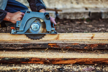 Circular saw for cutting boards into the hands of the builder, the man sawed bars, construction and home renovation, repair and construction tool. Carpenter Using Circular Saw for wood