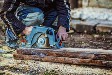 Circular saw for cutting boards into the hands of the builder, the man sawed bars, construction and home renovation, repair and construction tool. Carpenter Using Circular Saw for wood. Close-up