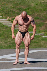 Obraz premium Powerful muscular bodybuilder in panties posing at the park. Quadriceps contraction